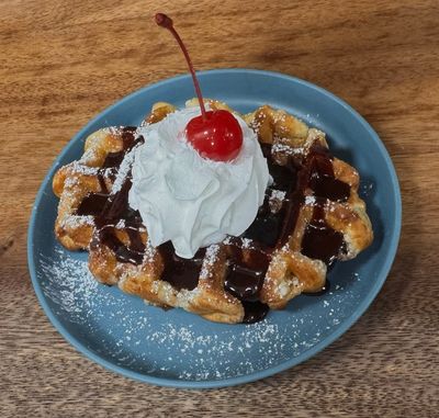 Belgium waffle topped with chocolate sauce, powdered sugar, whipped cream and a cherry